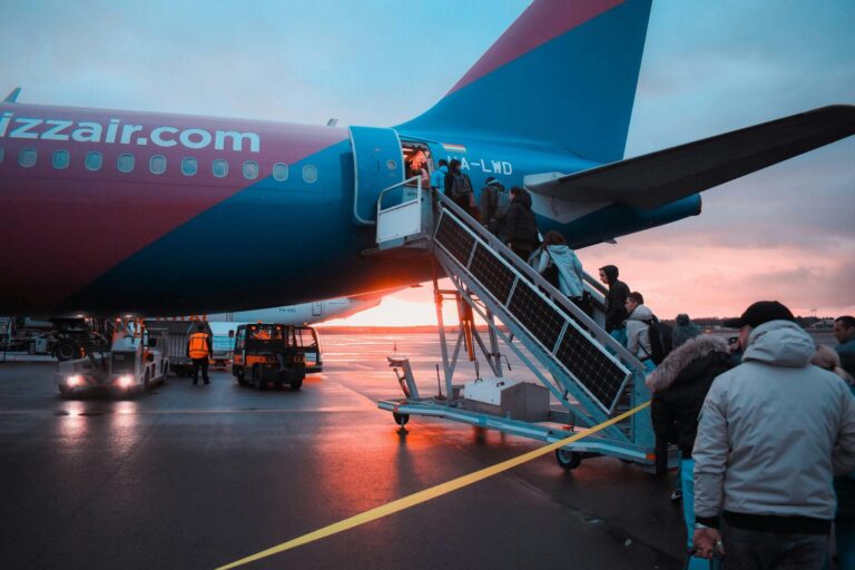 Passengers board a large blue and pink airplane via a stairway on an airport tarmac during sunset, utilizing quality pre-owned GSE equipment to ensure a smooth and efficient boarding process.
