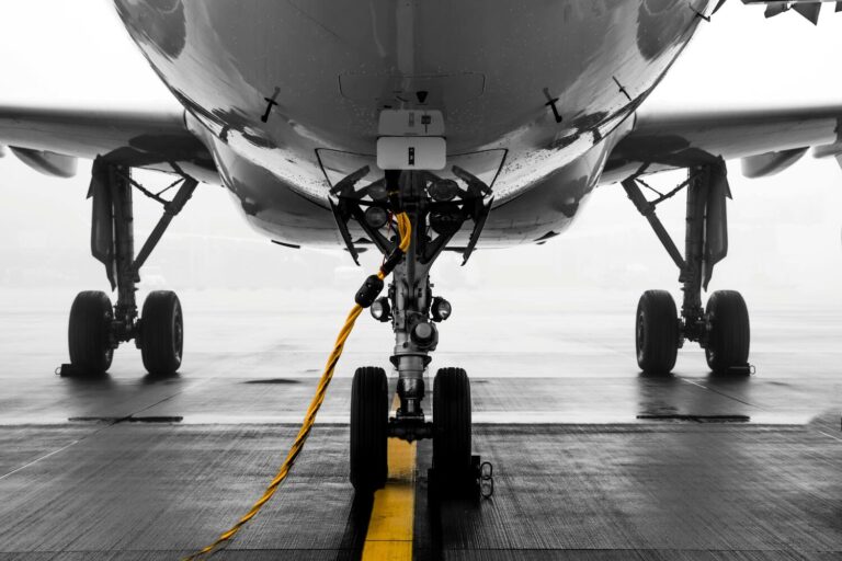 Close-up view of an airplane's landing gear on a tarmac, with a yellow tow bar attached, showcasing the reliability of quality pre-owned GSE.