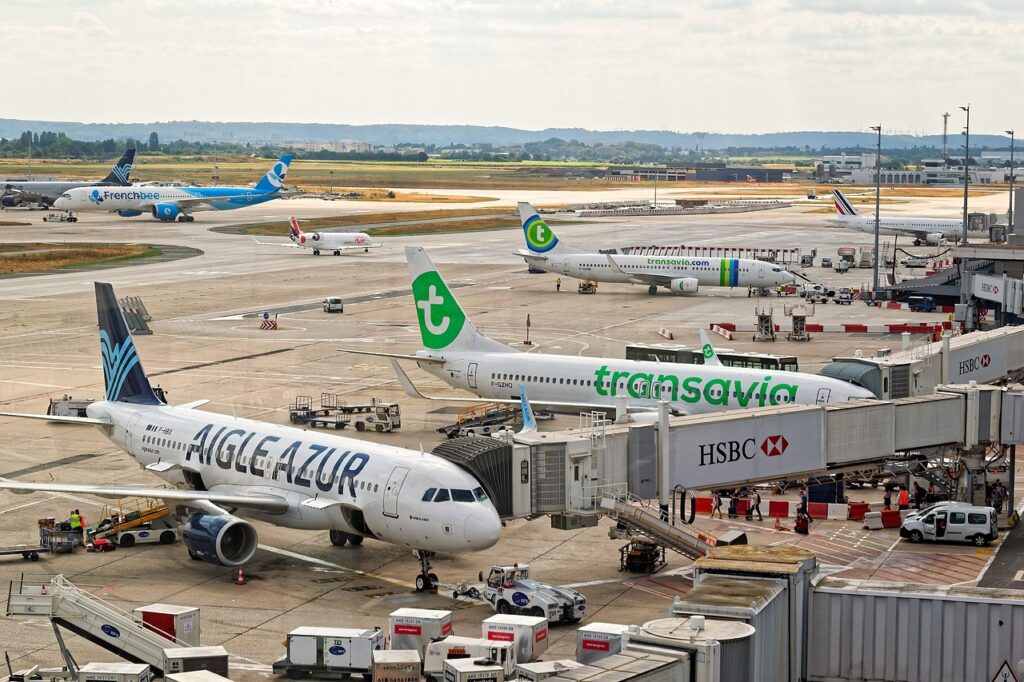 Airplanes from various airlines parked at airport gates, with ground service vehicles nearby and a view of the runway in the background.