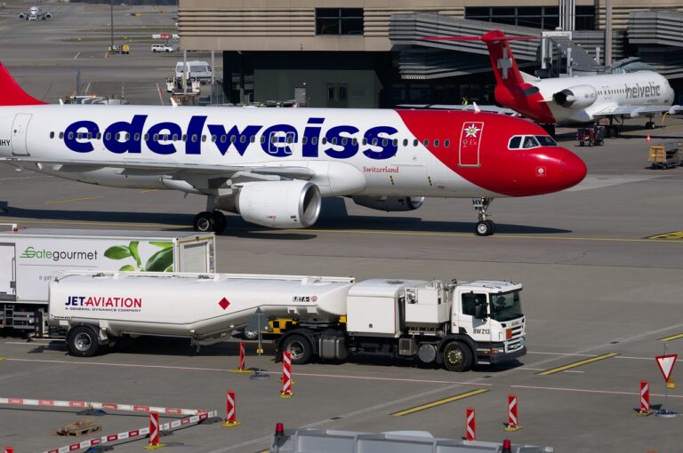 Two airplanes are parked at an airport gate, with a fueling truck in the foreground.