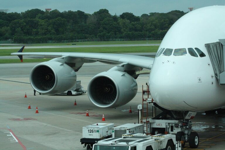 Close-up of a large airplane with two visible engines parked at an airport gate, with ground service equipment nearby.